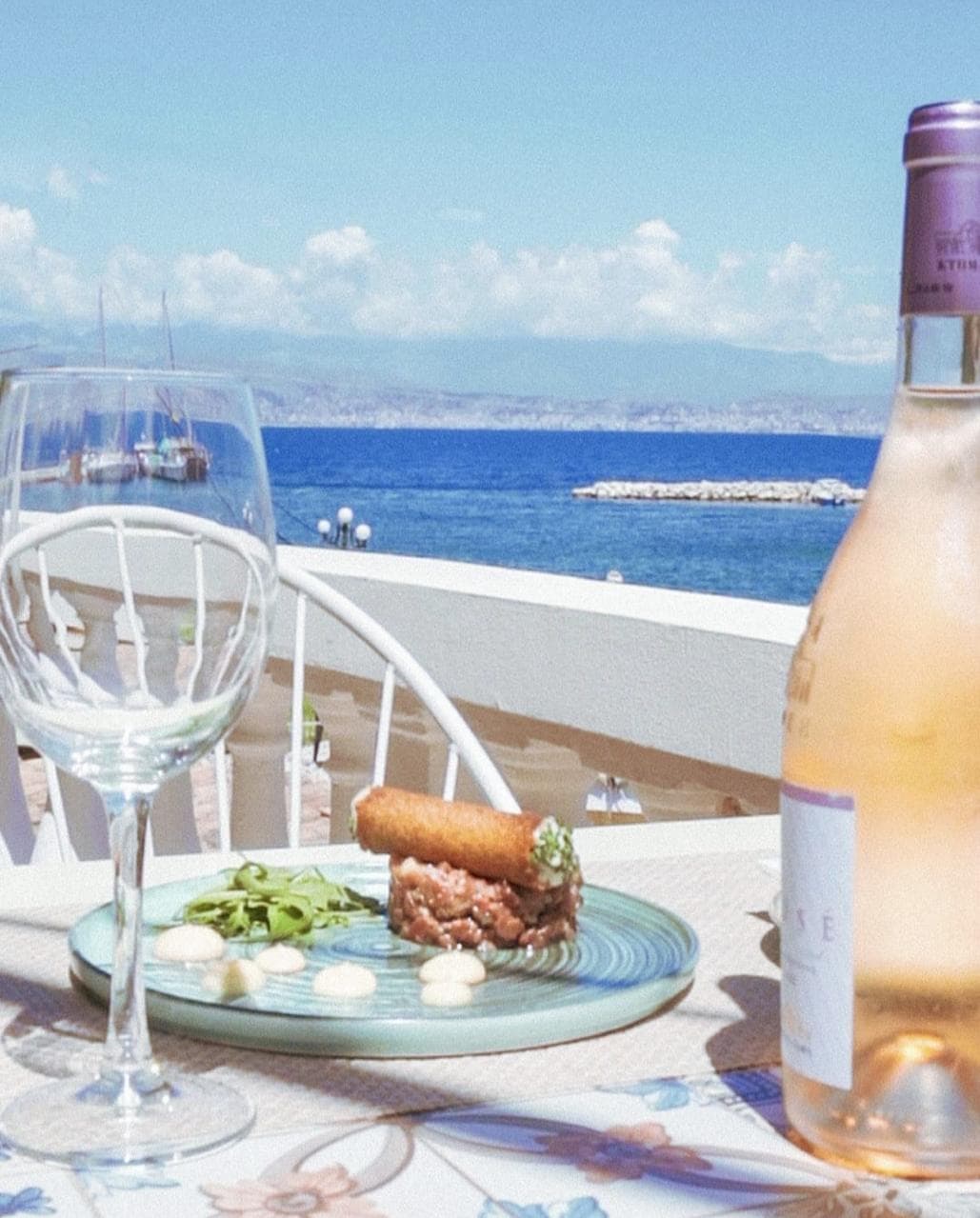 A glass and bottle of rosé on the table, the strait beyond