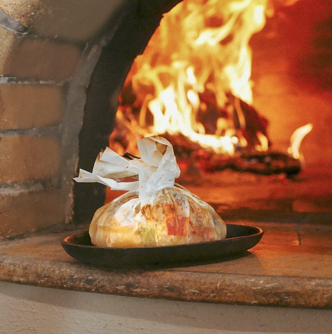 Wood-fired oven — paper-wrapped parcel cooking over flames